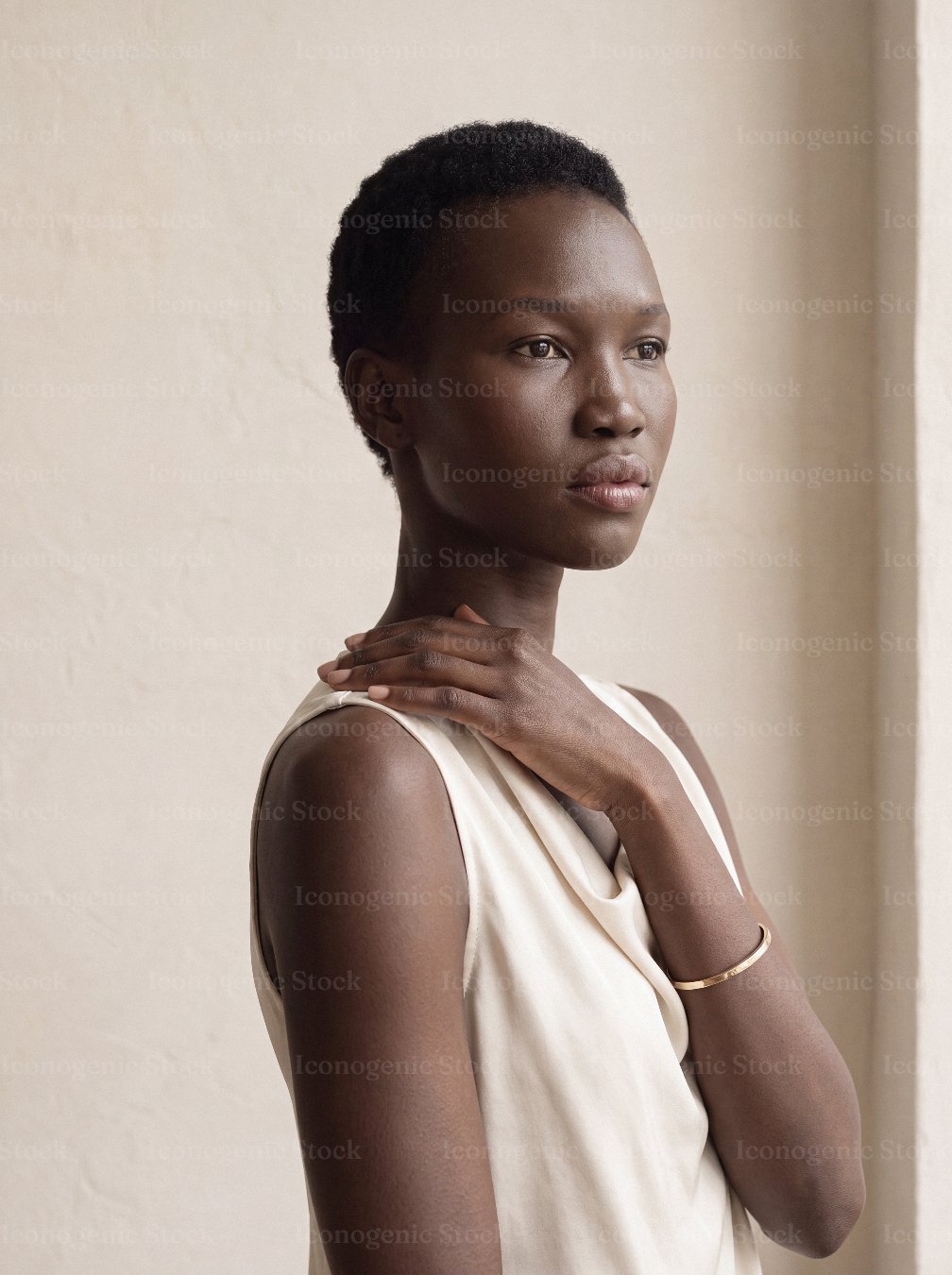 Elegant African woman in cream dress with gold bracelet gazing away