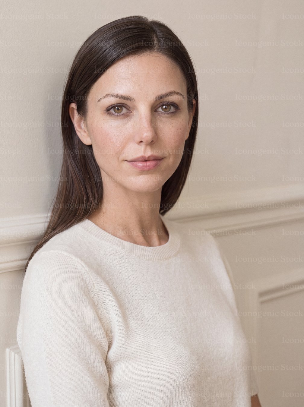 Confident woman with brown hair in cream sweater against neutral wall portrait