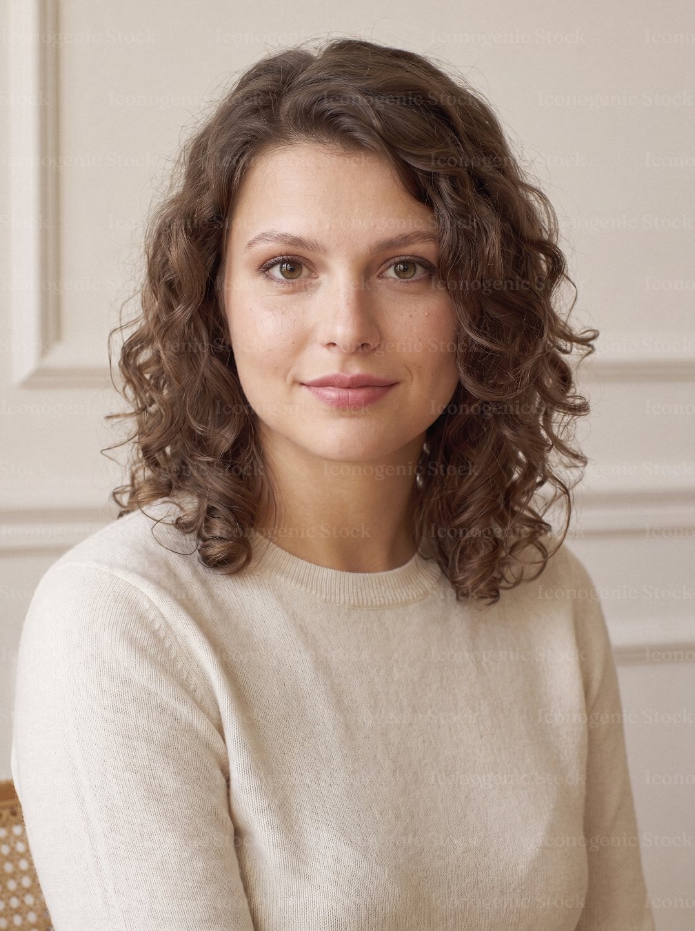 Portrait of smiling young woman with curly brown hair in cream sweater