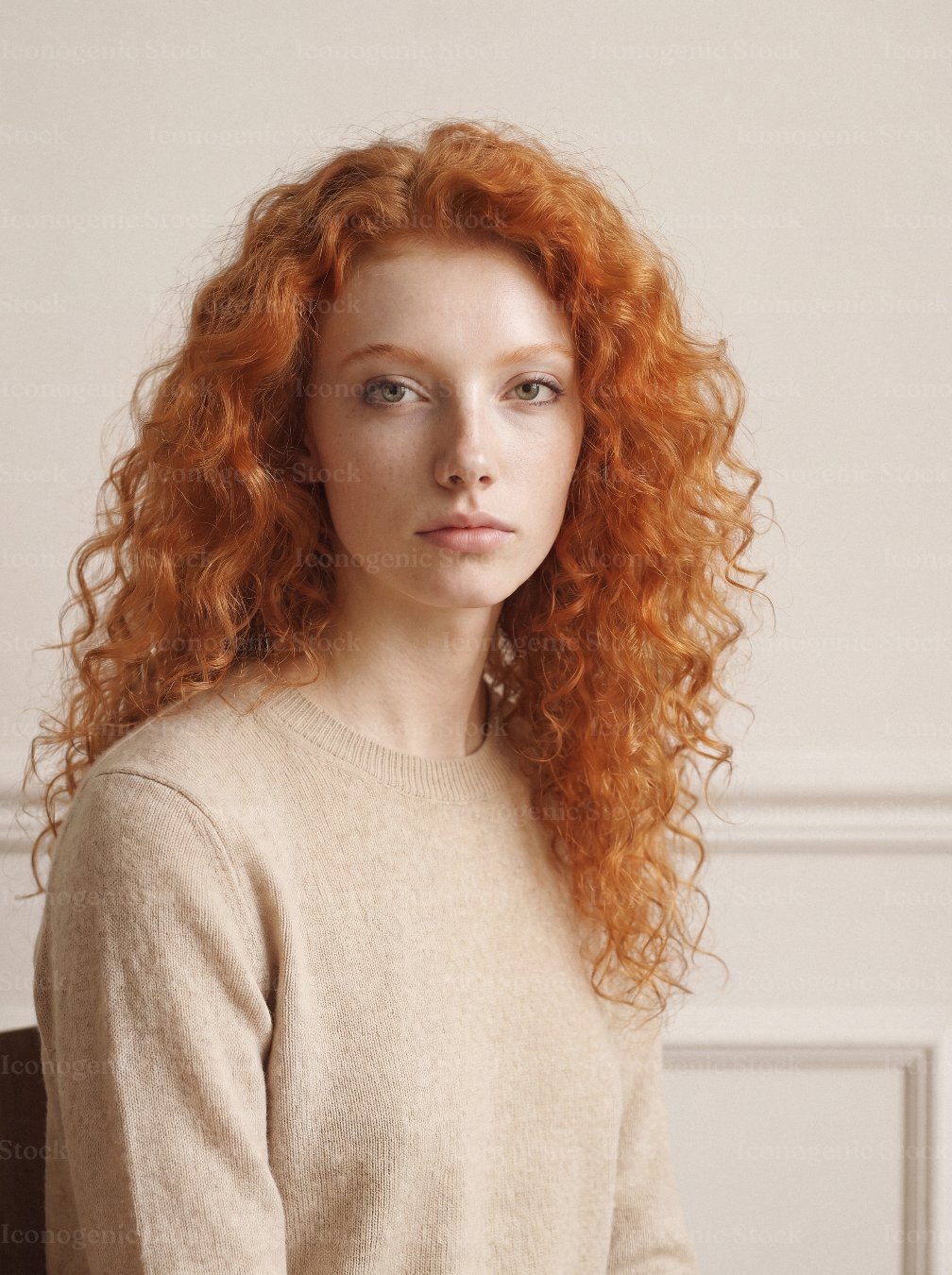 Portrait of young woman with curly red hair wearing beige sweater indoors