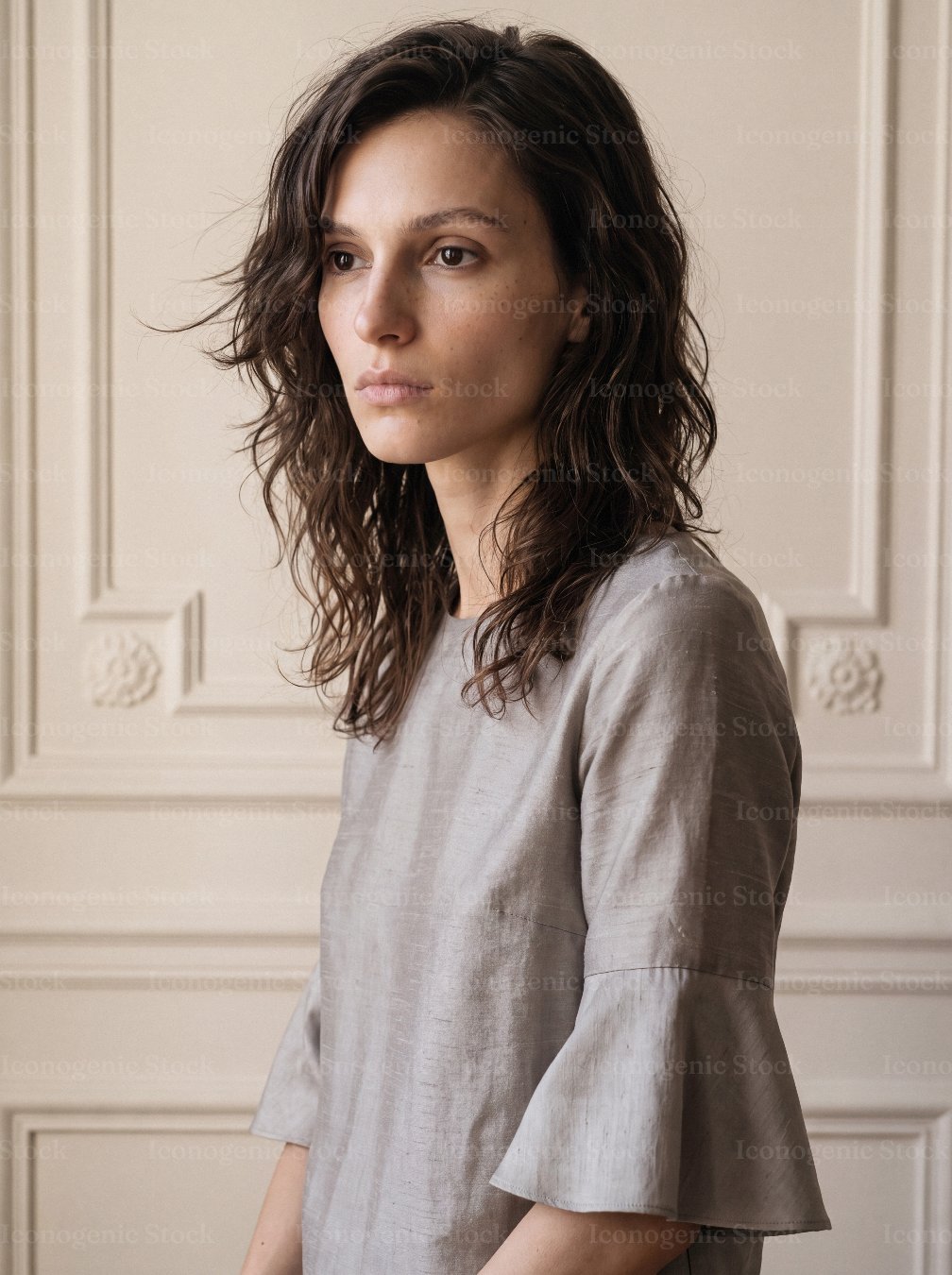 Portrait of woman with wavy hair wearing gray blouse against classic wall paneling