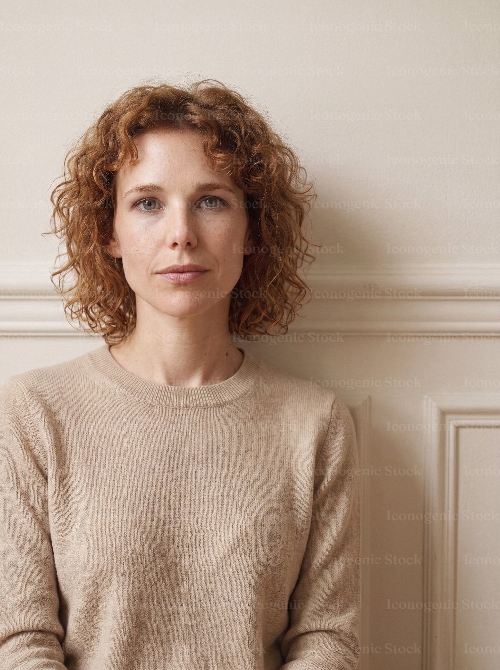 Portrait of a woman with curly red hair wearing a beige sweater indoors