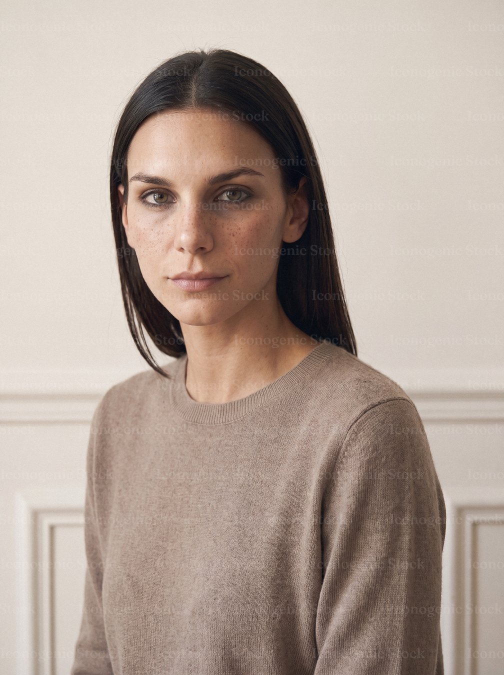 Natural portrait of a young woman with dark hair and freckles in beige sweater