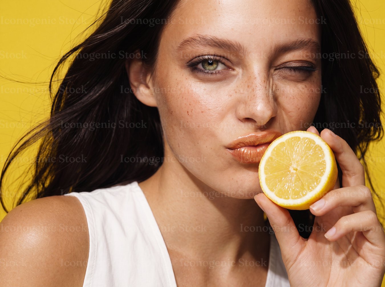 Winking woman holding a fresh lemon half against a yellow background