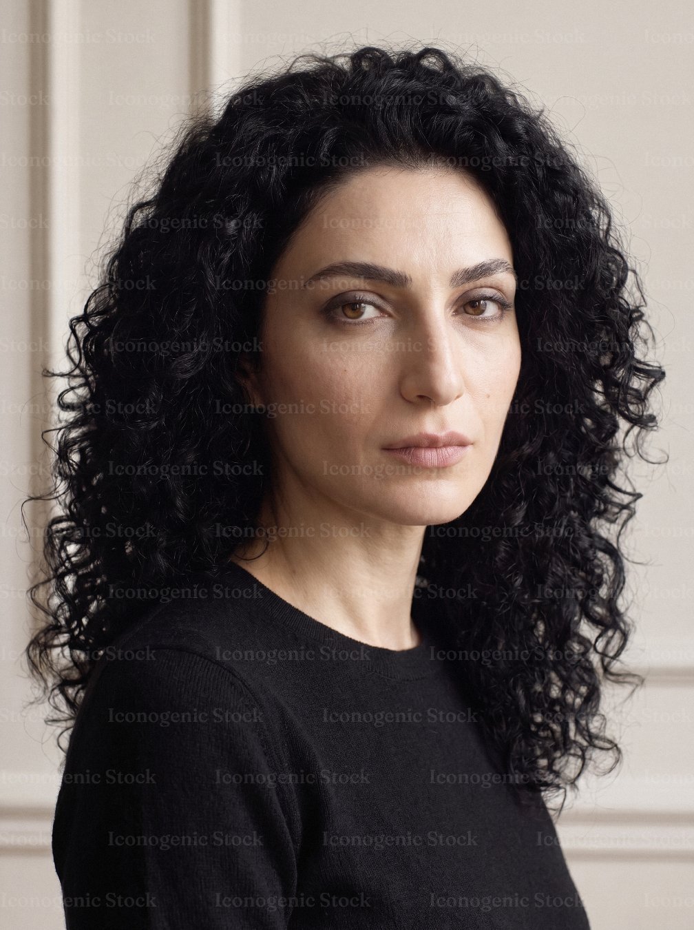 Confident woman with curly dark hair looking at camera in studio portrait