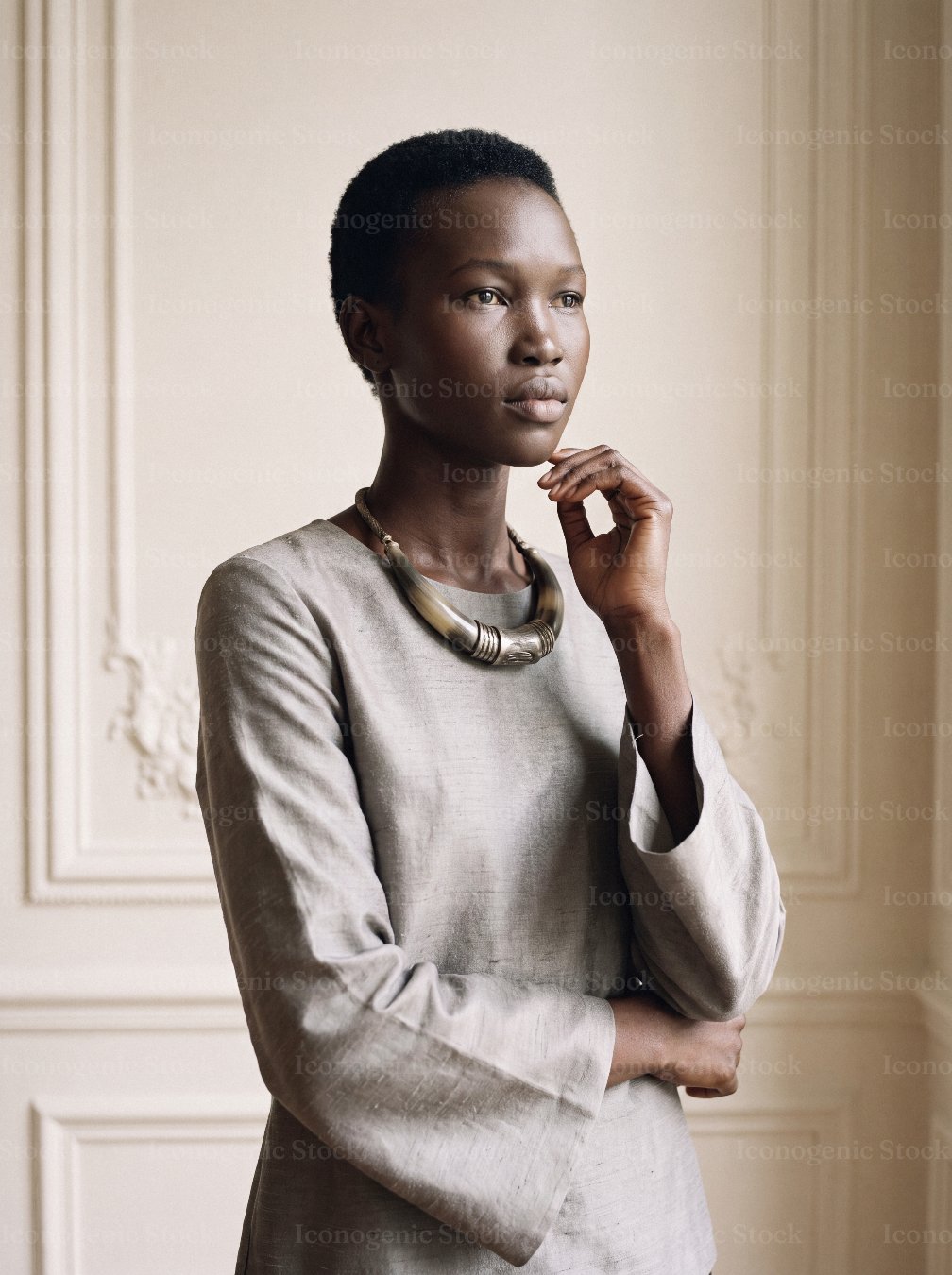 Elegant African woman in gray tunic with statement necklace, thoughtful pose indoors