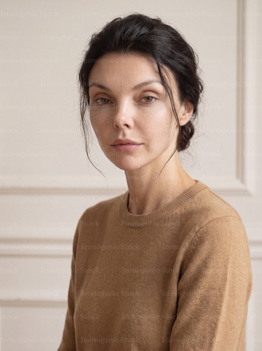 Serene woman with dark hair in beige sweater, natural portrait against soft wall