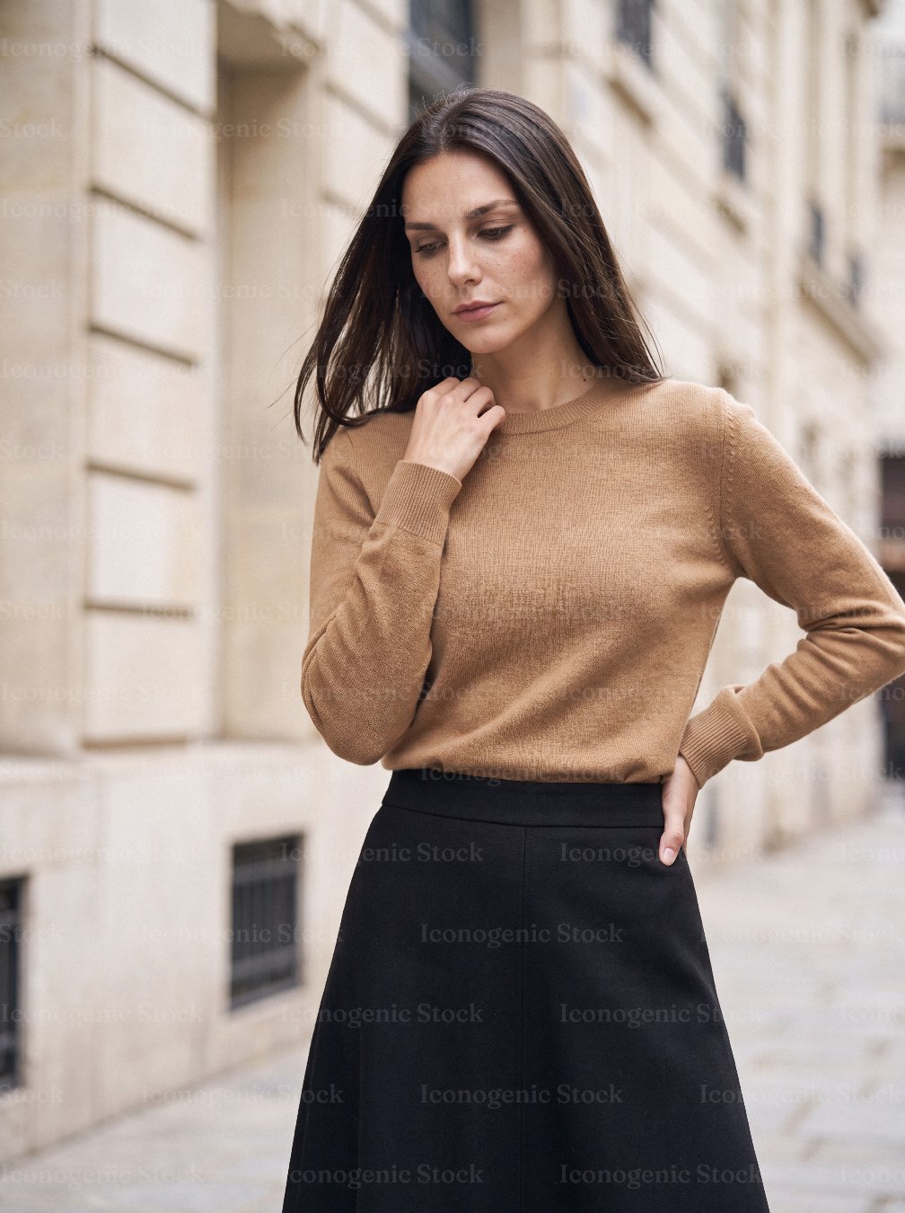 Elegant woman in camel sweater and black skirt standing on city street