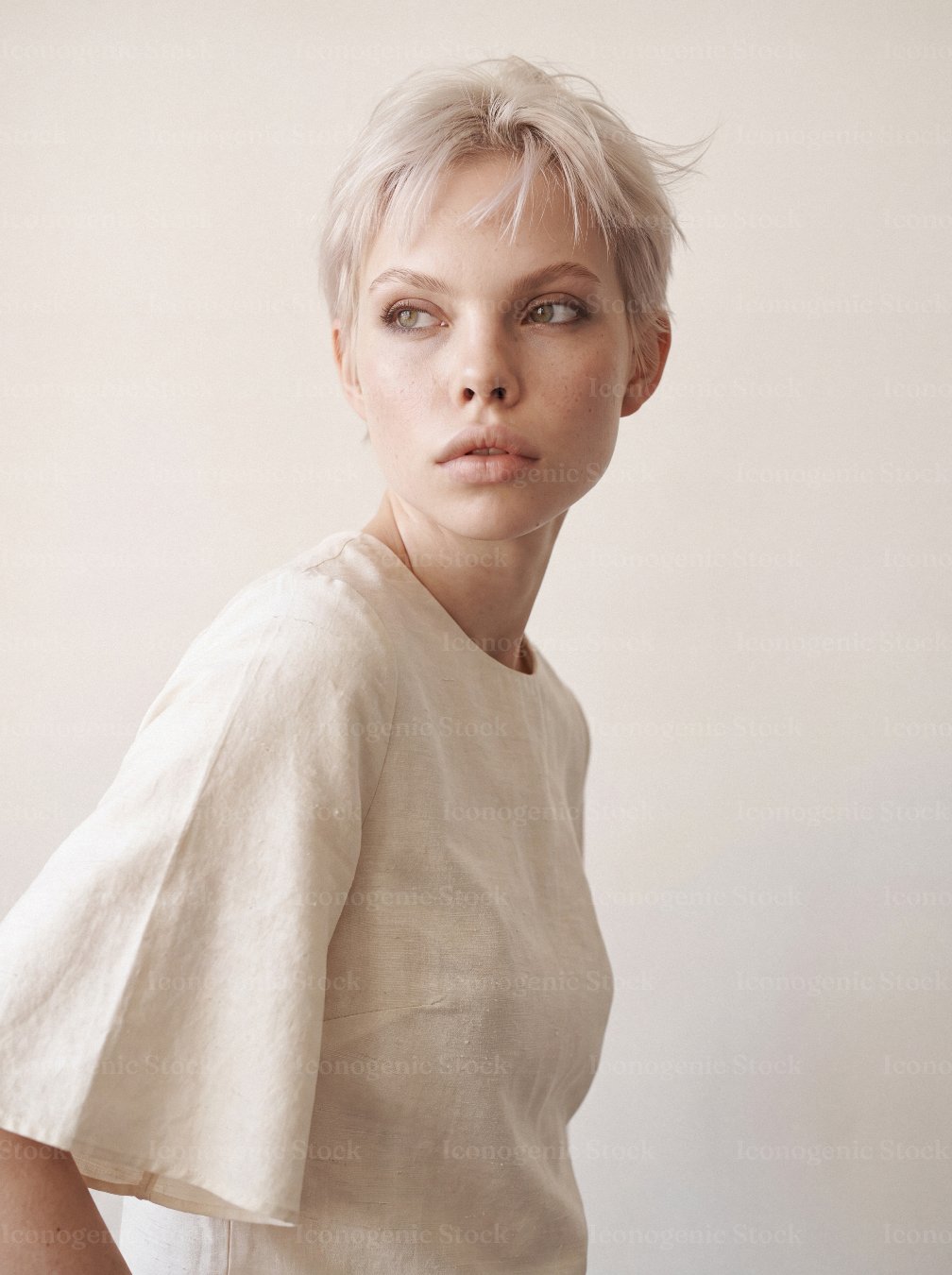 Young woman with platinum pixie haircut wearing beige linen blouse, studio portrait