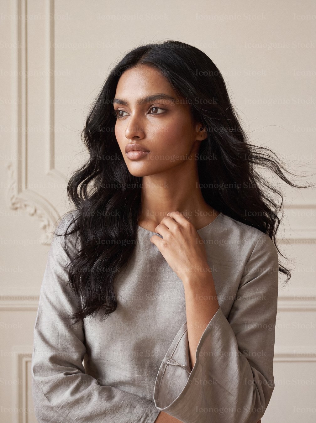 Elegant young woman with long wavy dark hair in silky grey blouse indoors
