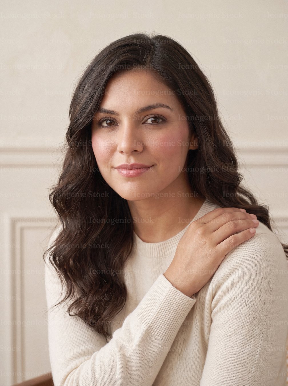 Portrait of confident young woman with wavy hair in cream sweater, neutral background