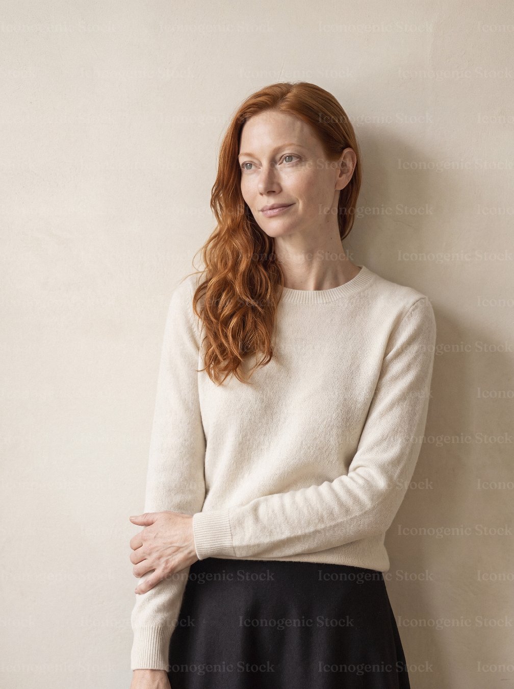 Portrait of redhead woman in cream sweater standing against neutral wall, looking away thoughtfully