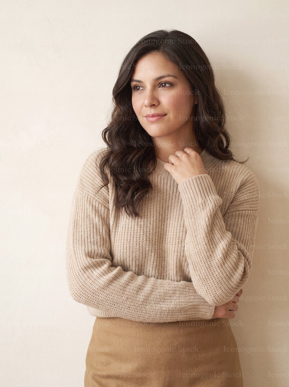 Young woman in beige knit sweater looking sideways against neutral wall