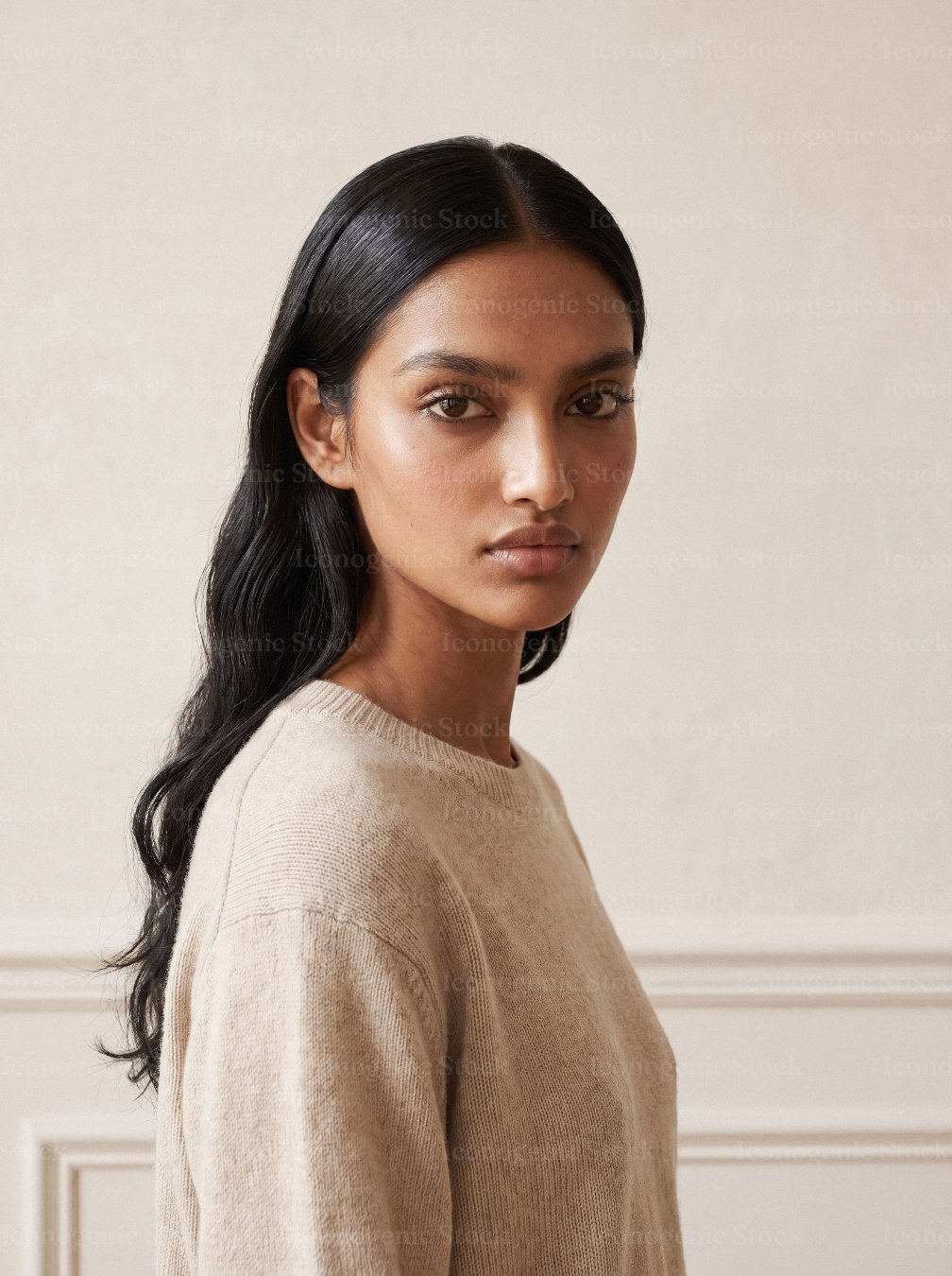 Young woman with long dark hair wearing a beige knit sweater, looking at camera
