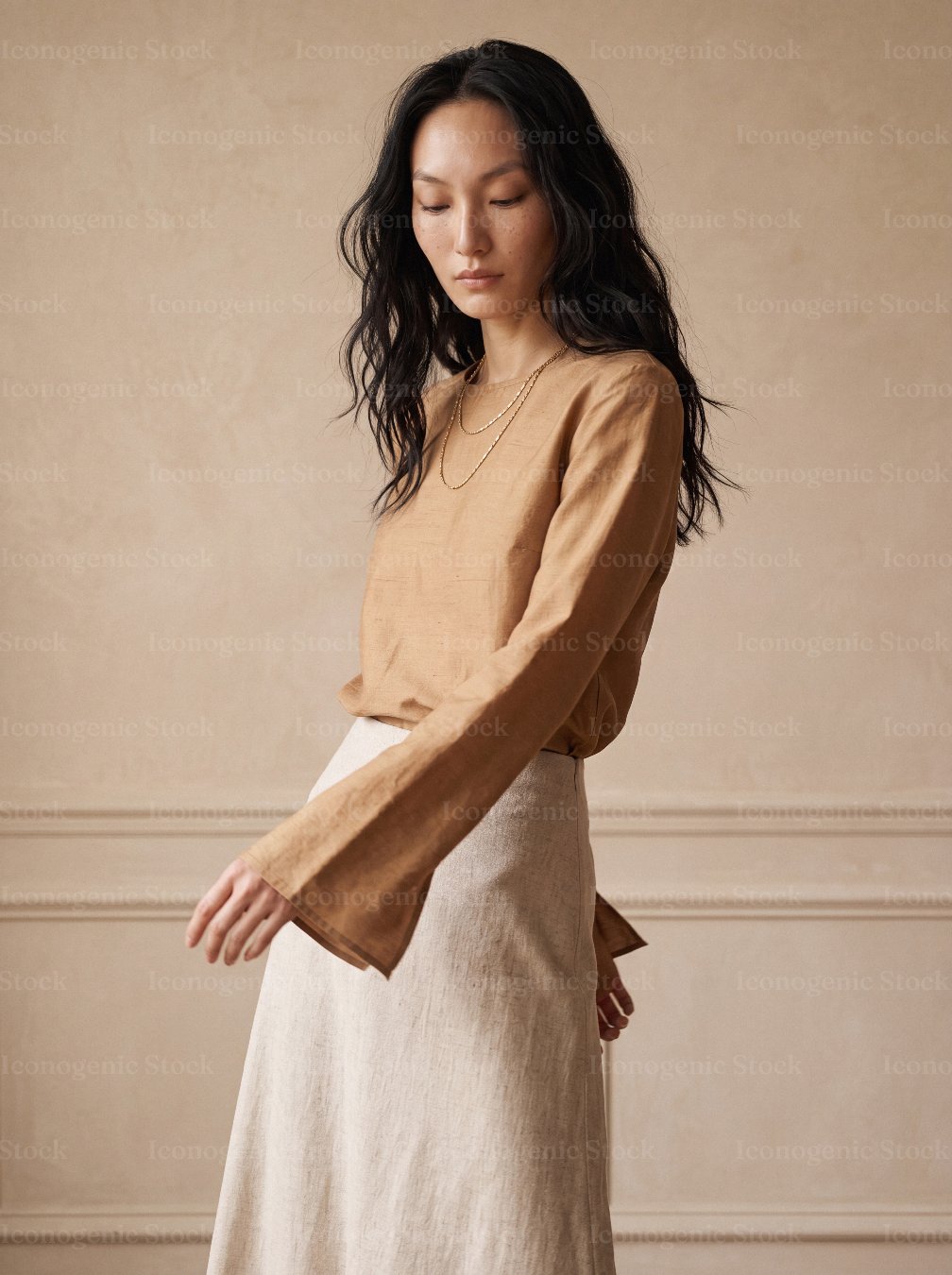 Asian woman in tan blouse and beige skirt posing against neutral wall