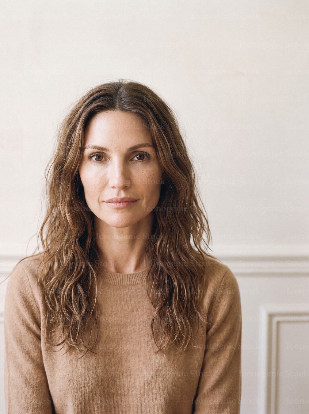 Natural portrait of woman with wavy brown hair in cozy beige sweater indoors