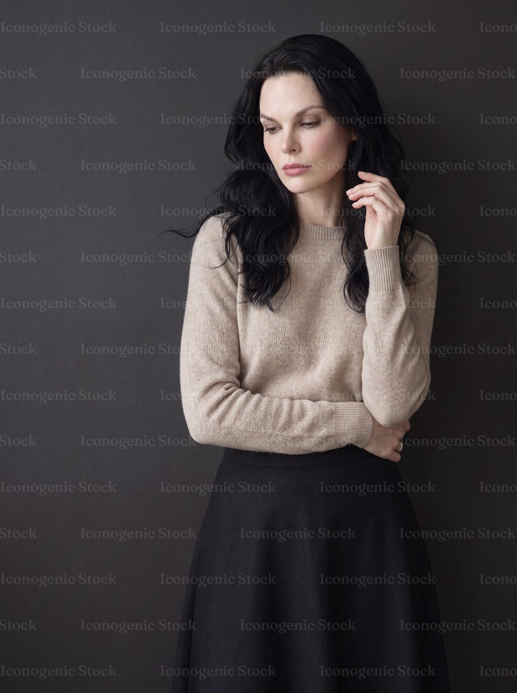 Elegant woman with dark hair in beige sweater posing thoughtfully against dark background
