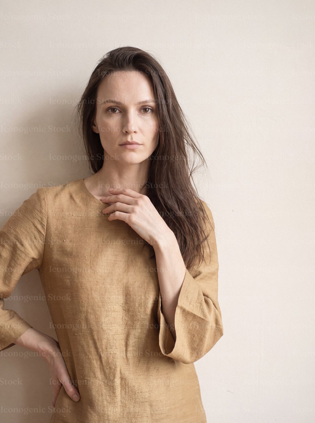 Serene woman in beige linen dress standing against neutral wall, minimalist portrait