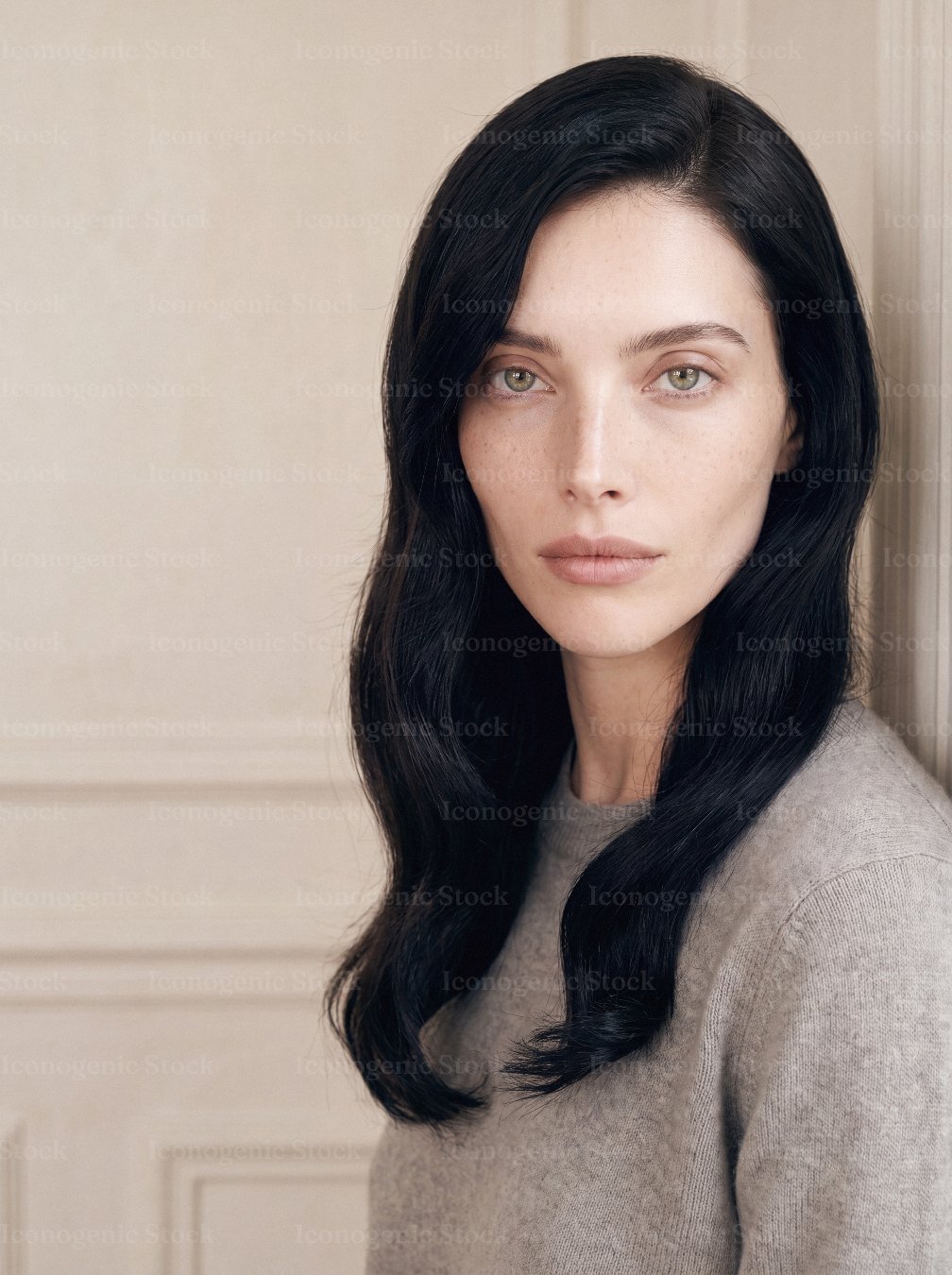 Portrait of young woman with long black hair and green eyes in neutral sweater