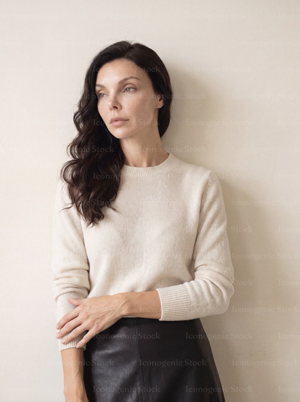 Elegant woman in cream sweater and leather skirt against neutral wall