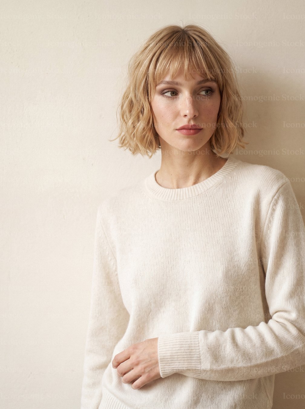 Young woman with blonde bob haircut wearing cream knit sweater against beige wall