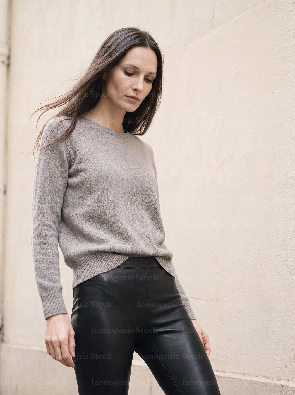 Woman in taupe cashmere sweater and leather leggings standing by wall