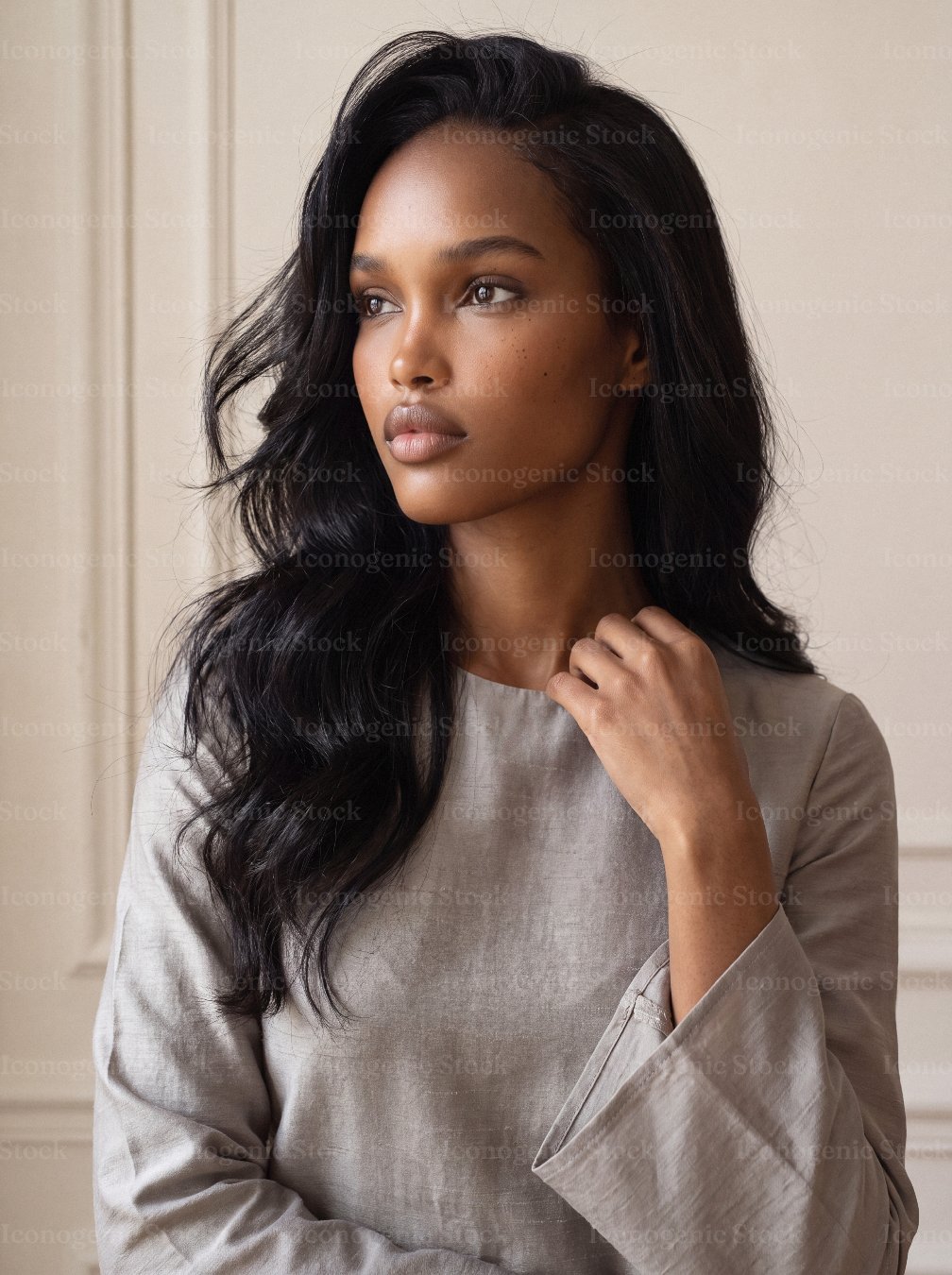 Elegant young woman with long wavy hair in neutral tone blouse, contemplative gaze