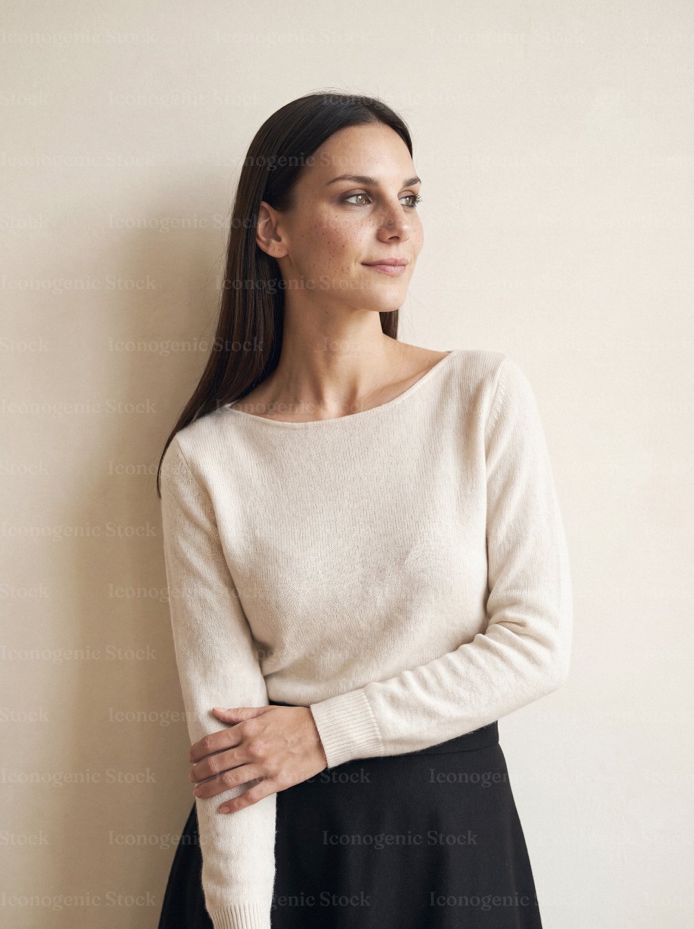 Elegant woman in cream sweater standing against neutral wall looking away
