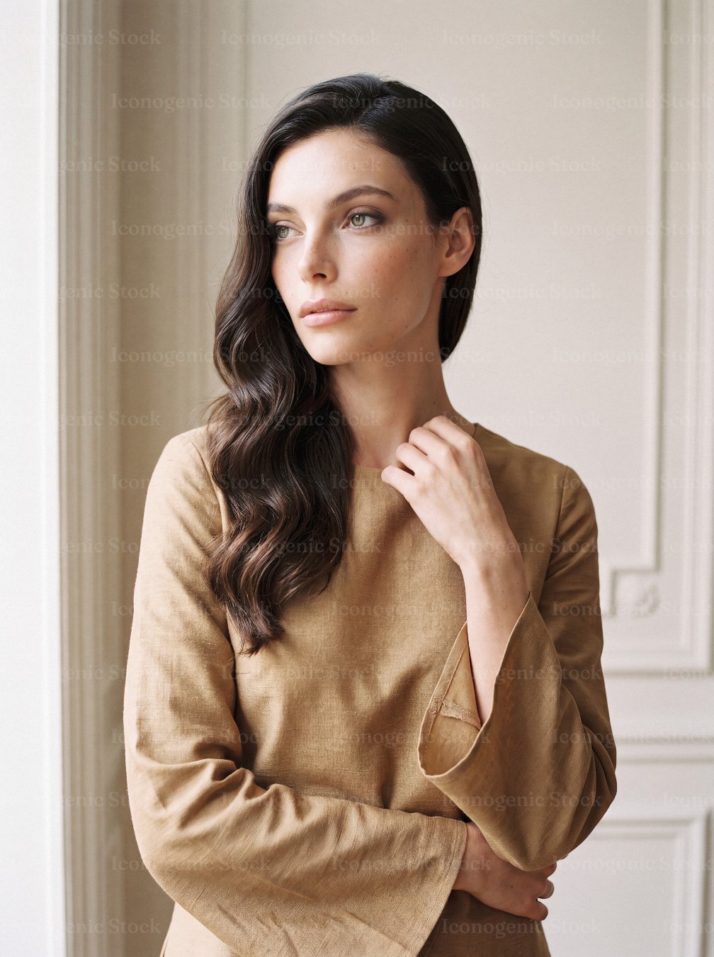Elegant brunette woman in beige linen dress standing by window in classic interior