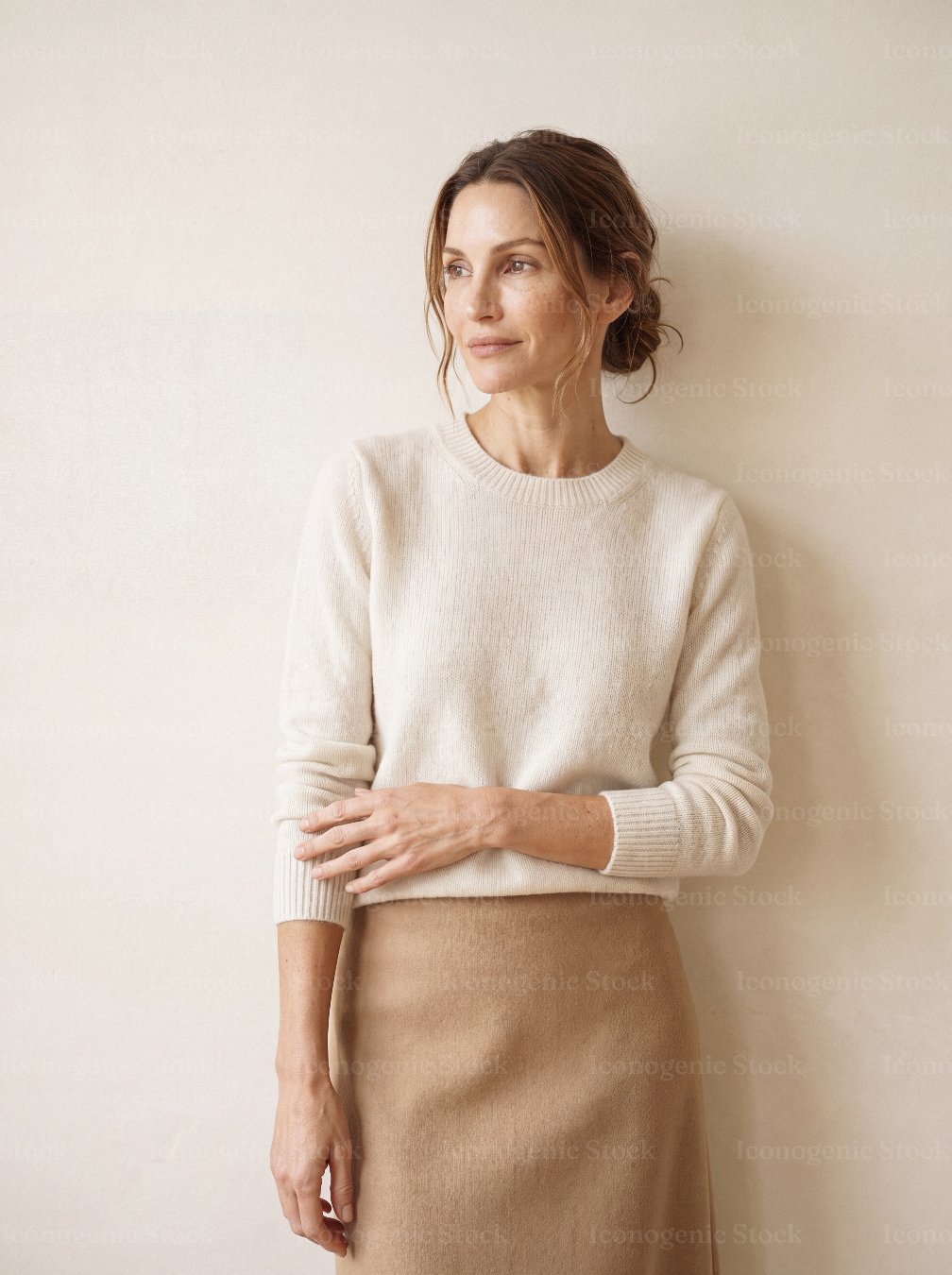 Elegant woman in cream sweater and beige skirt standing against neutral wall