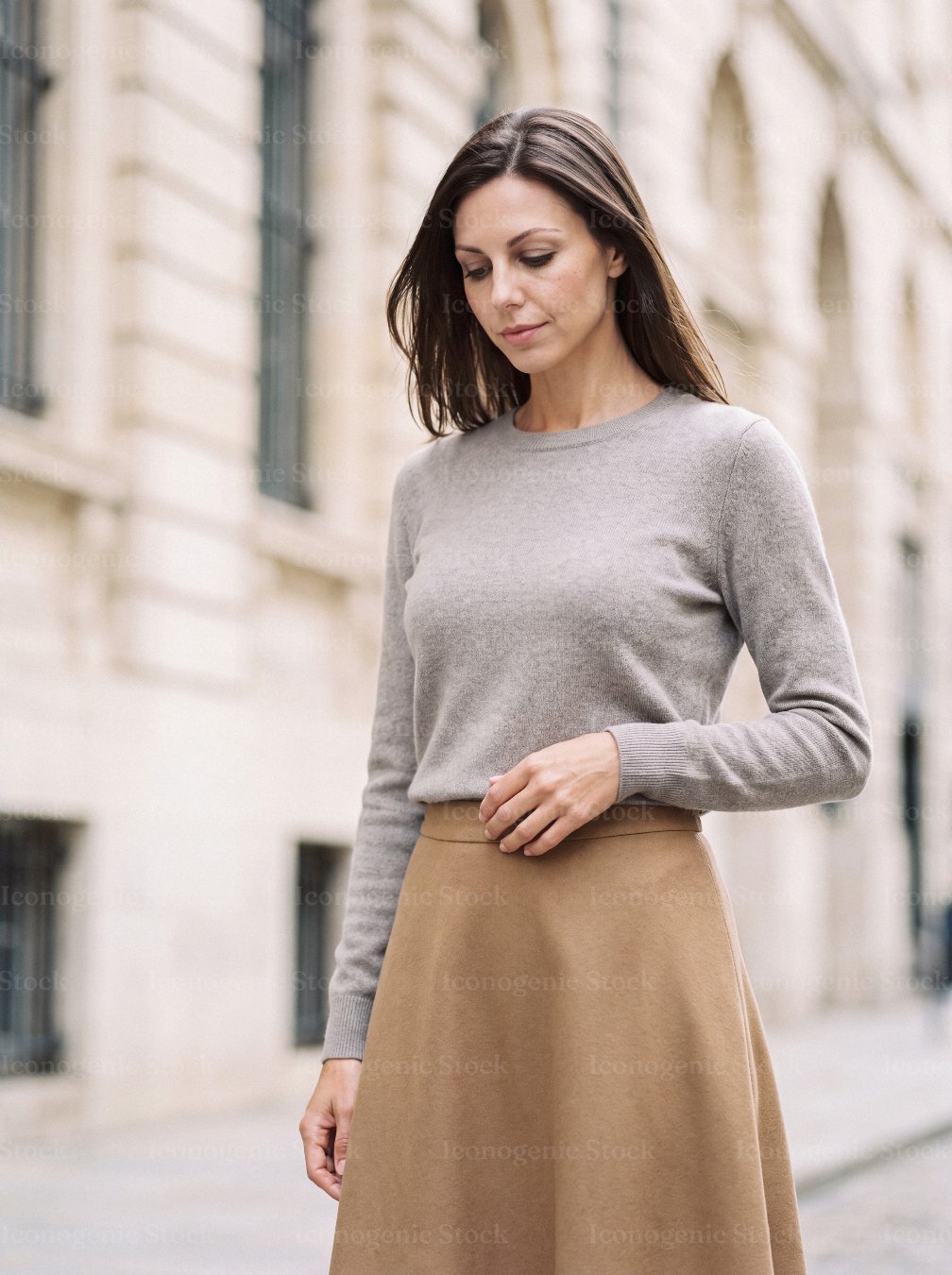 Elegant woman in gray sweater and camel skirt walking on city street