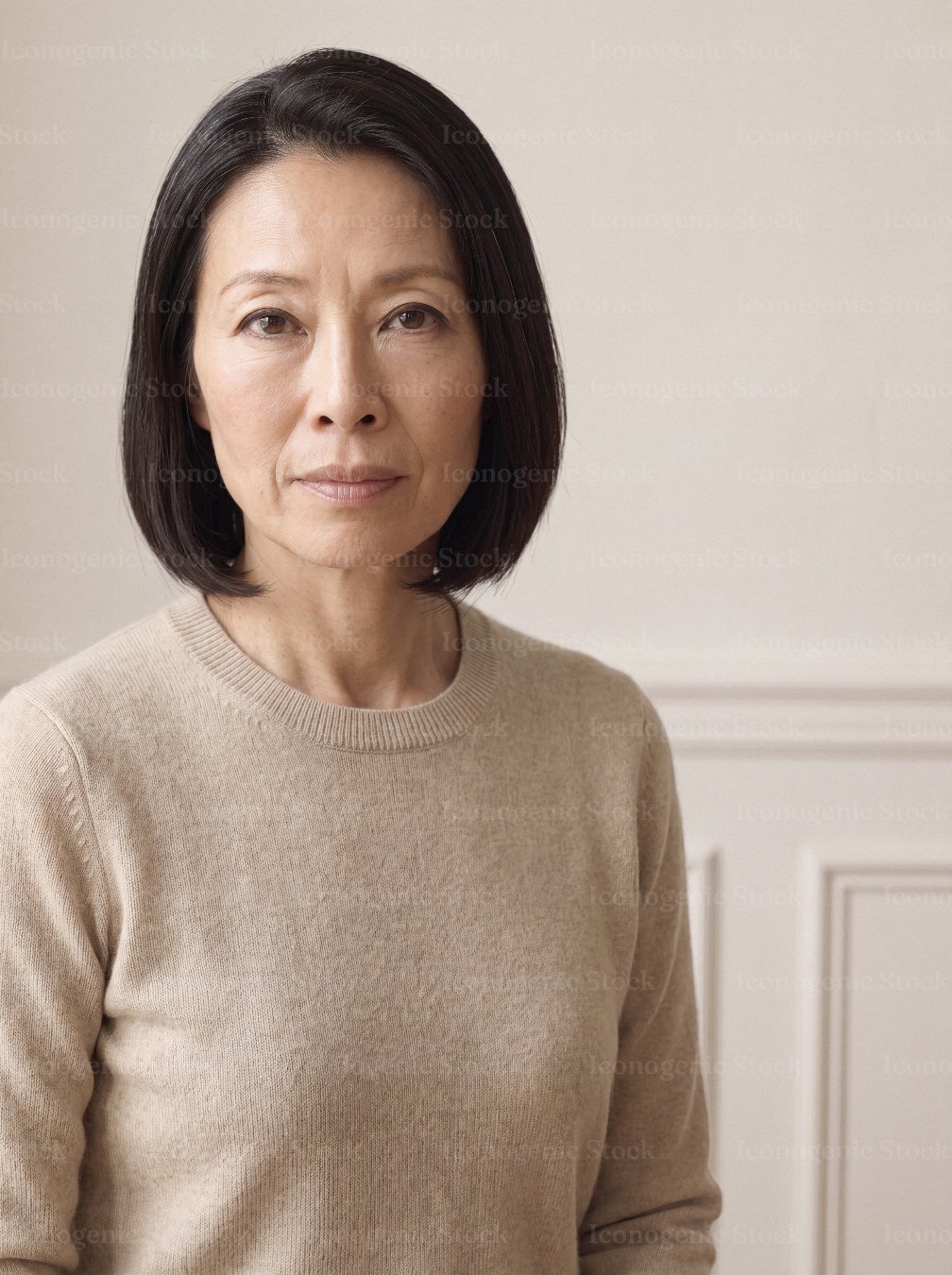 Portrait of a mature Asian woman in a beige sweater against neutral wall