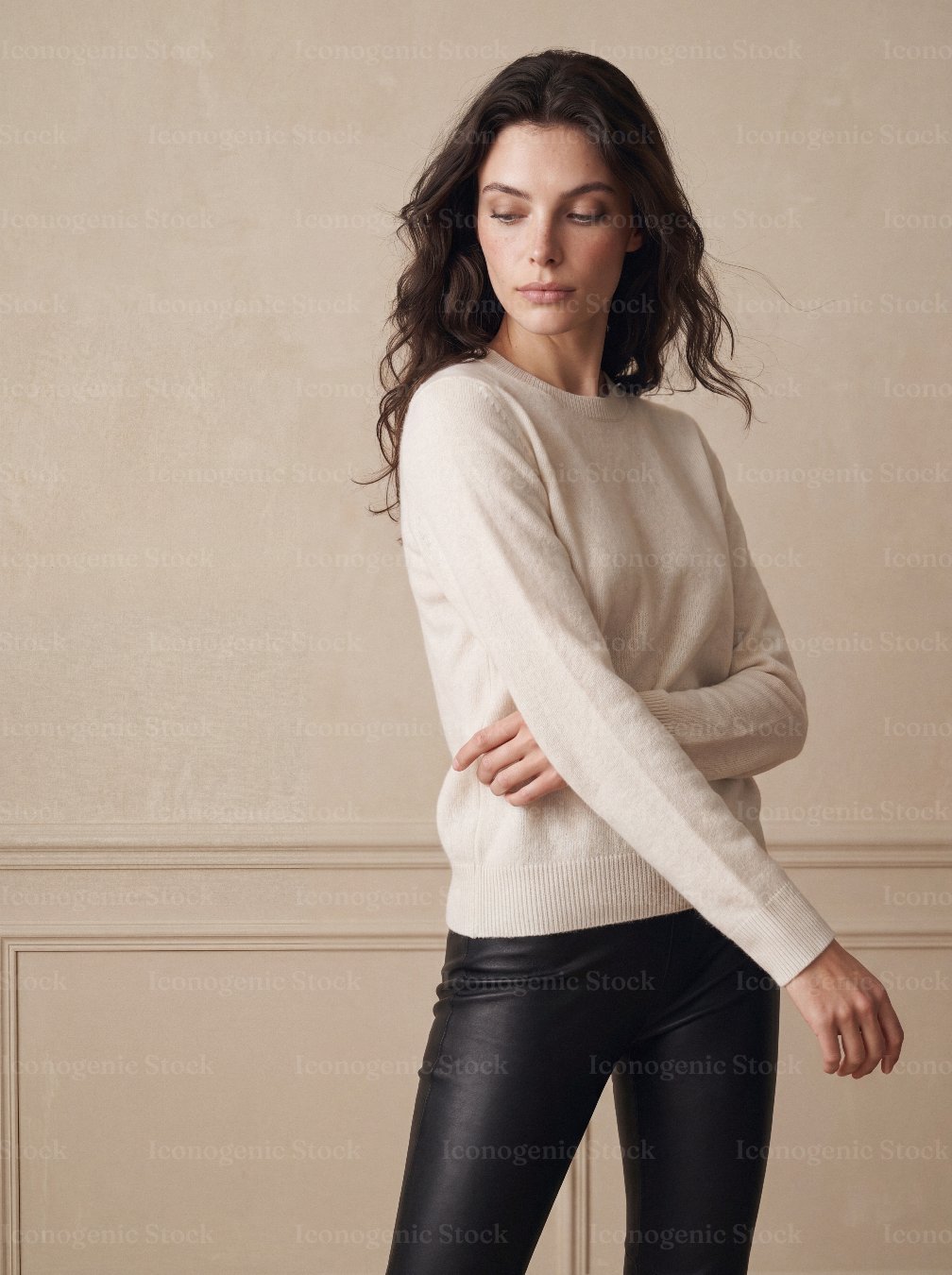Elegant woman in cream sweater and black leather pants against beige wall