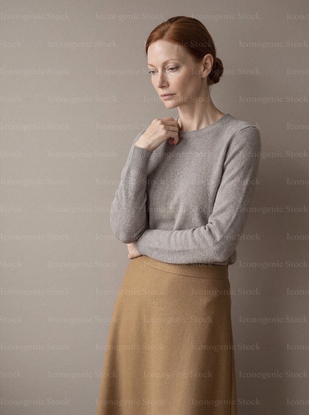 Elegant redhead woman in beige sweater and camel skirt against neutral wall