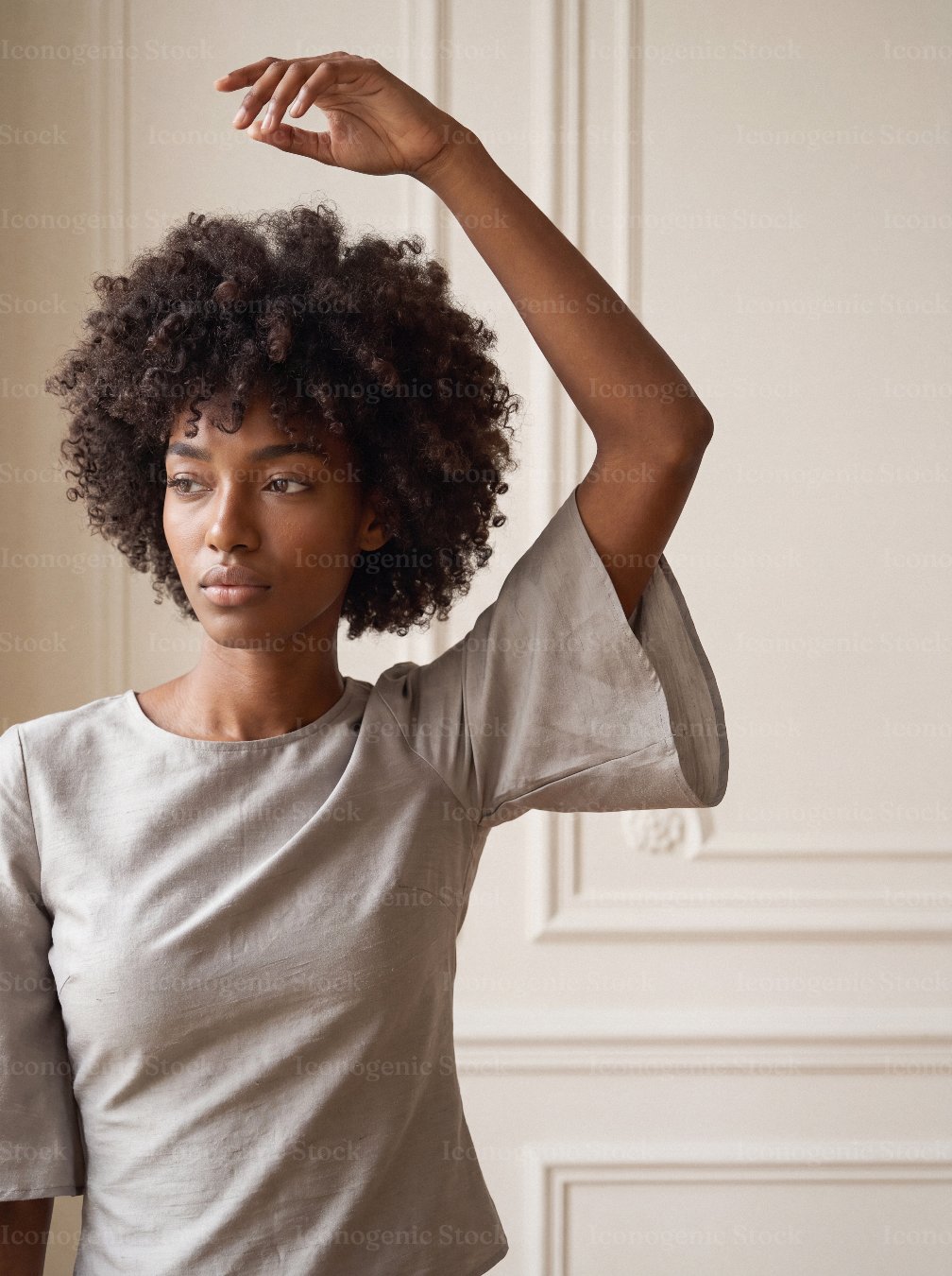 Young woman with curly afro hair raising arm in elegant neutral top